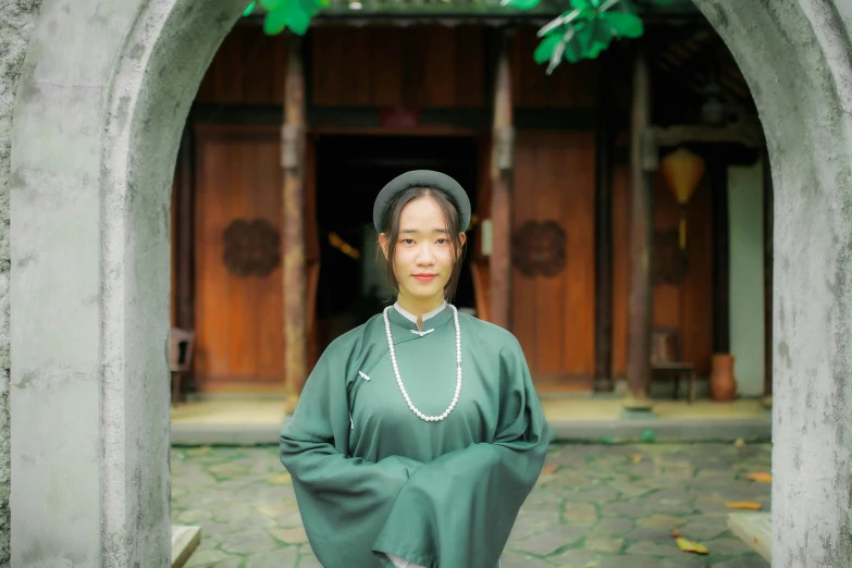 a woman standing in front of a stone archway wearing a green dress and a chain around her neck