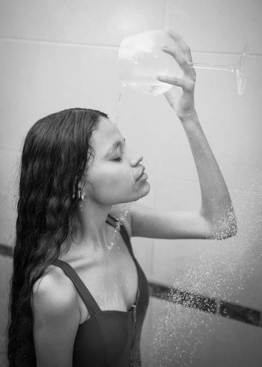 a young woman in a wet - tiled room, holding a sprayer over her head while looking down at the water flowing out from the faucet