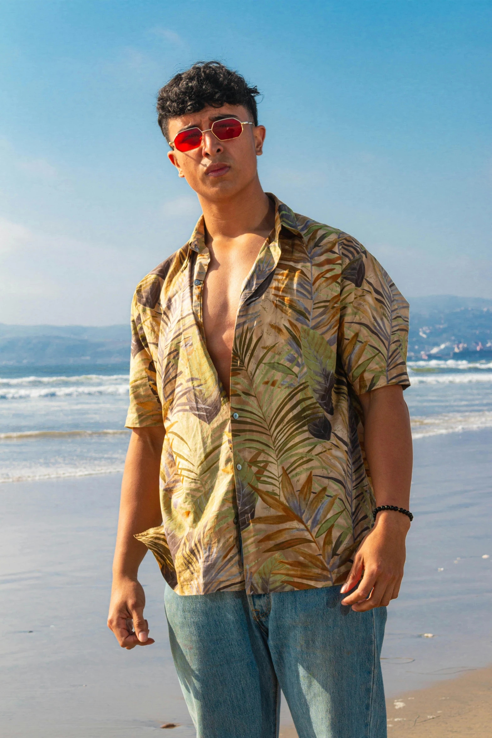 man with sunglasses standing on the beach and staring at the camera