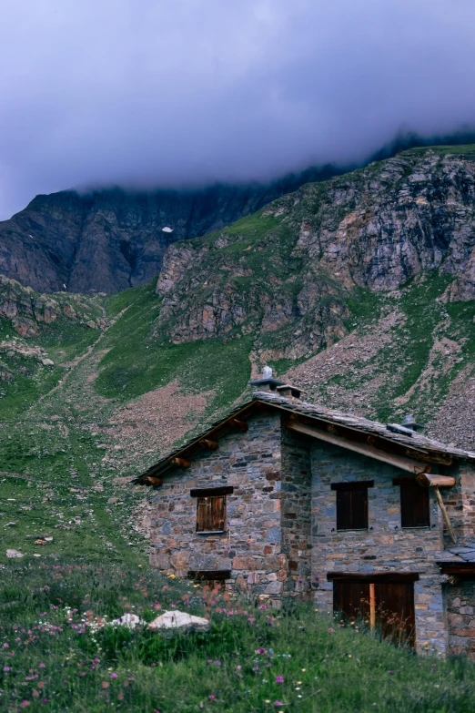 the stone cabin is in a field near the mountain