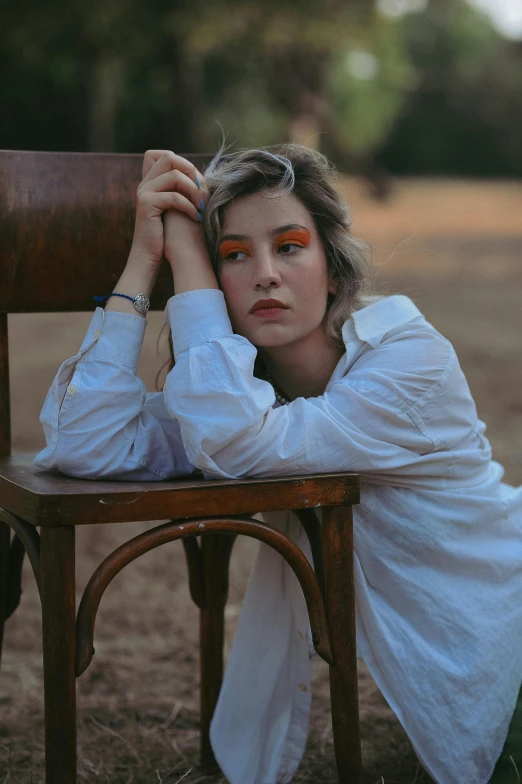 a woman with orange makeup poses for a portrait on a chair