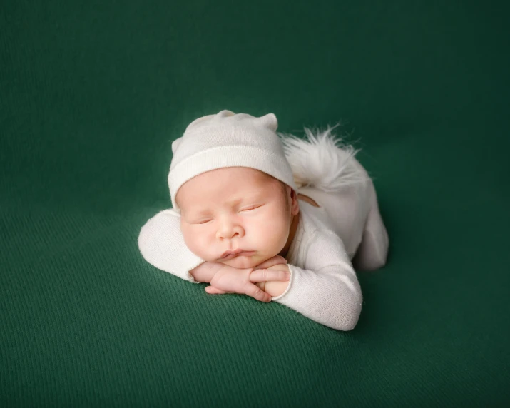 a small baby laying on a green blanket wearing a hat