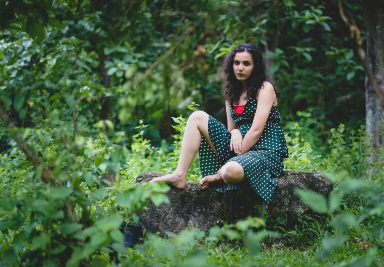 a young lady sitting on top of a tree stump in the woods