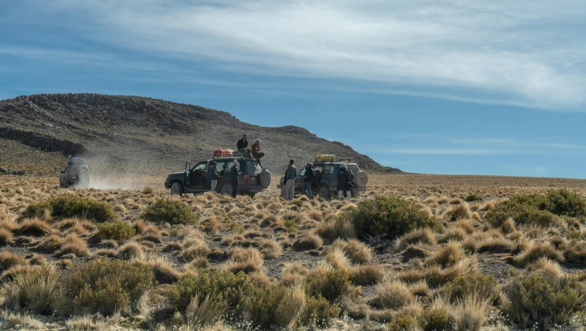 two green trucks driving through the desert next to a mountain