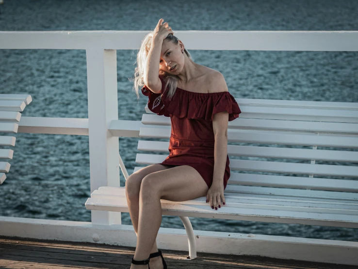 woman in red dress sitting on white bench near water