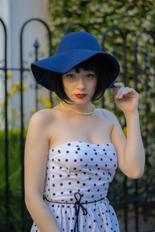 a woman wearing a hat while standing in front of a wrought fence