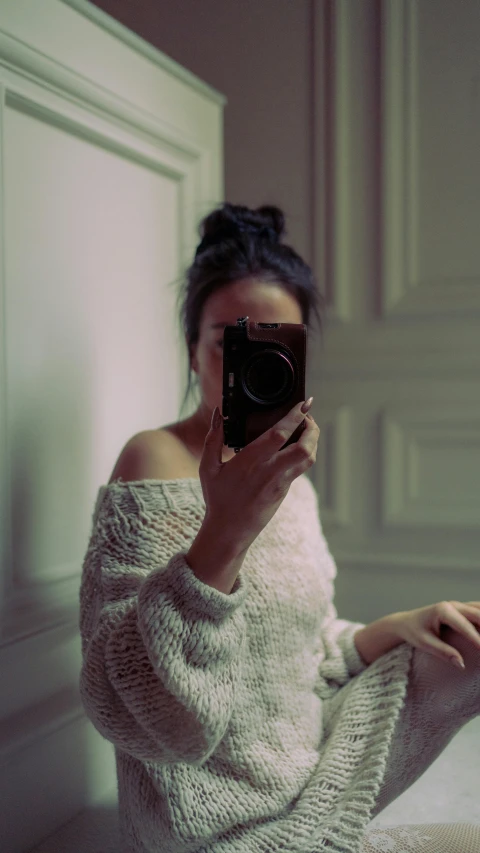 a woman sits in a room with her feet up taking a picture with a cell phone