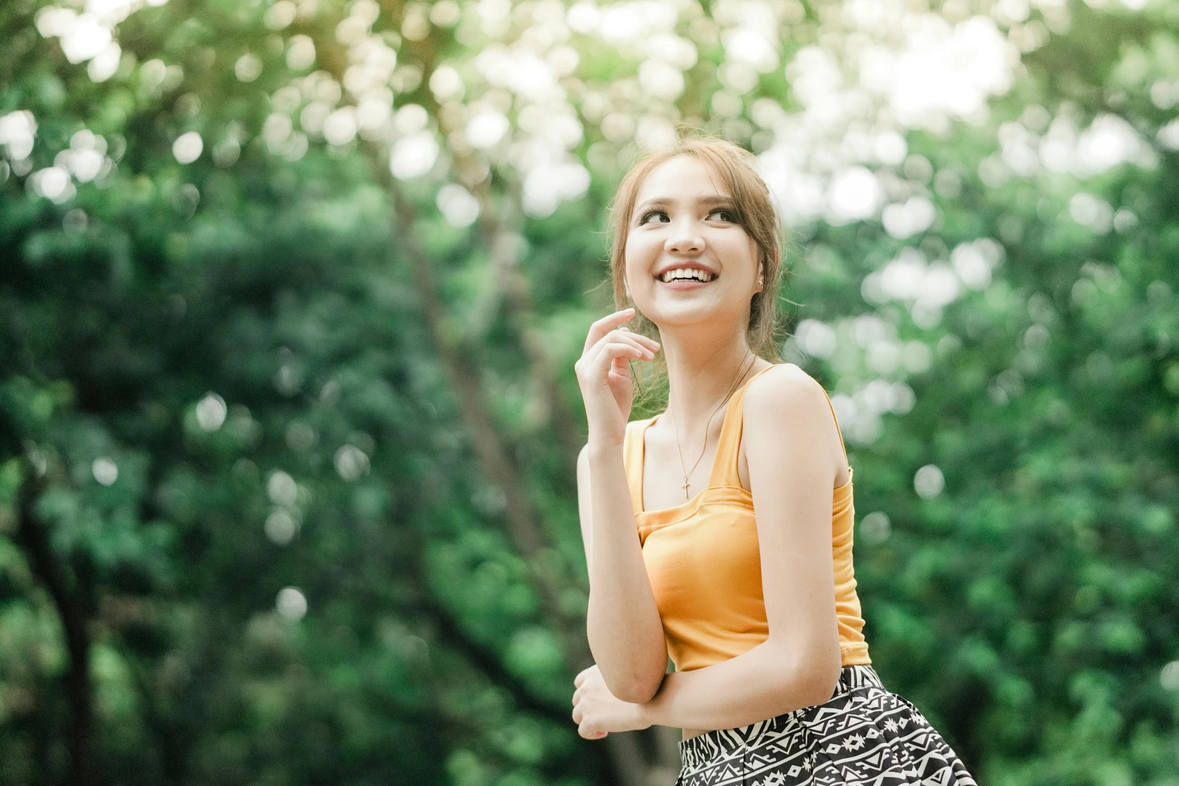 an asian woman smiling with trees and bushes behind her