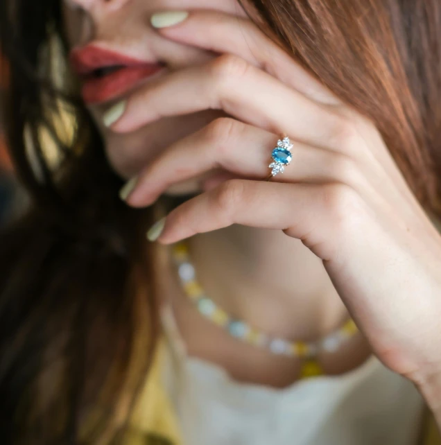 a woman with her hand to the face holding a piece of jewelry in her left hand