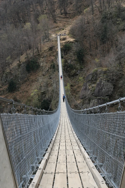 people walk over a large rope bridge that is suspended by chains