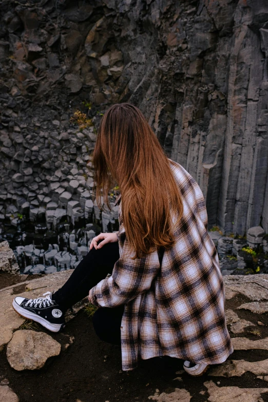 the person sits on a rocky ledge with long hair