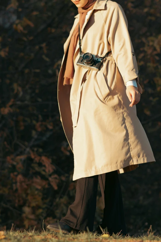 the woman is walking across a grassy field wearing a brown coat