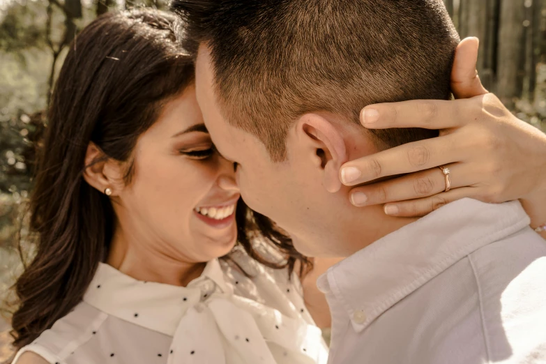 a beautiful couple cuddling each other in front of some trees