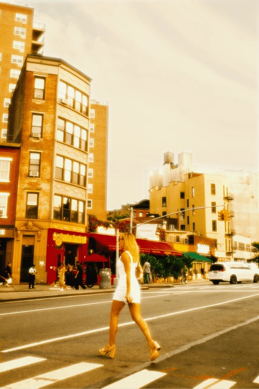 woman in white dress crossing street, tall buildings line background