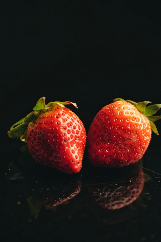 two strawberrys with green stems against a black background