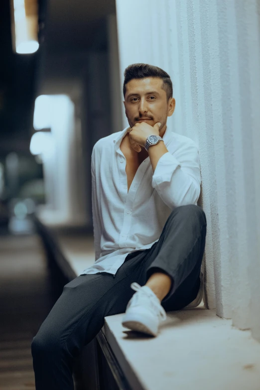 man sitting on wall with white shirt, black pants and tennis shoes