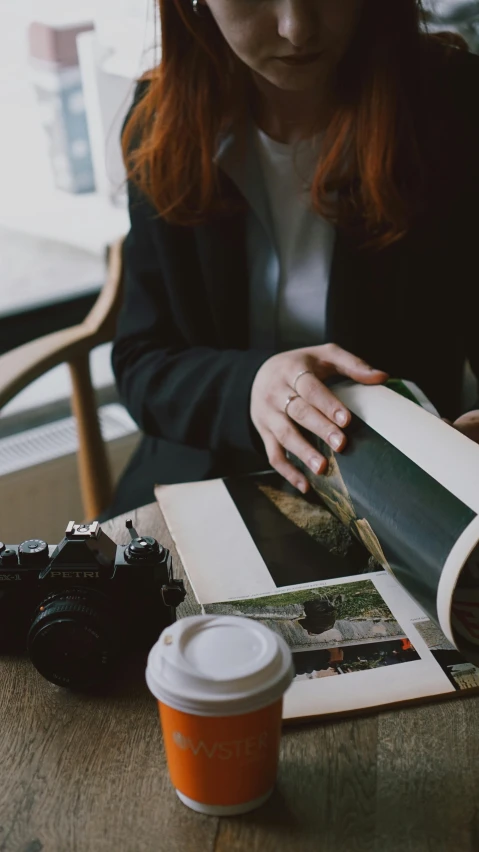 a woman with red hair sitting in front of a magazine and orange coffee cup