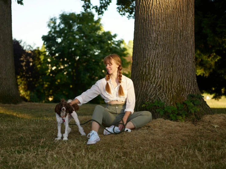 a woman in pants is holding a small dog next to a tree