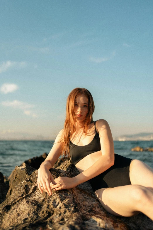 a beautiful woman sitting on top of a rocky shoreline