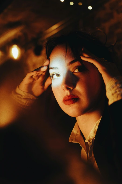 a woman is looking at her face while standing in front of a lamp