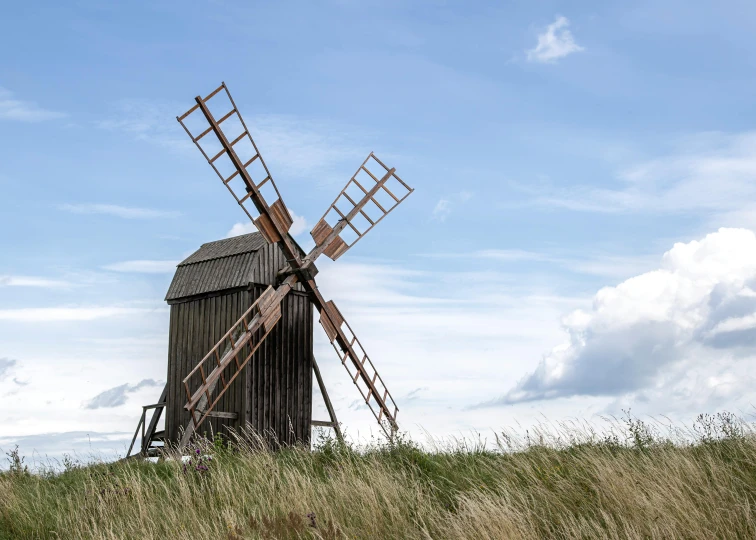 a brown windmill in the grass near a hill