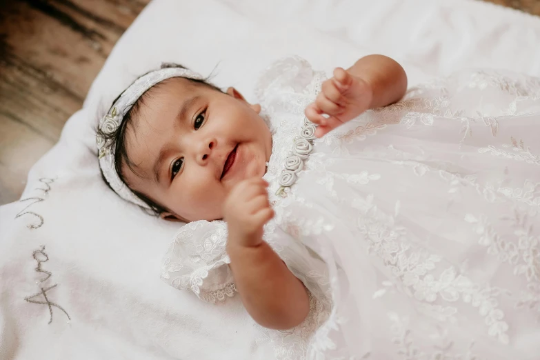 a baby dressed up in a white dress smiles for the camera