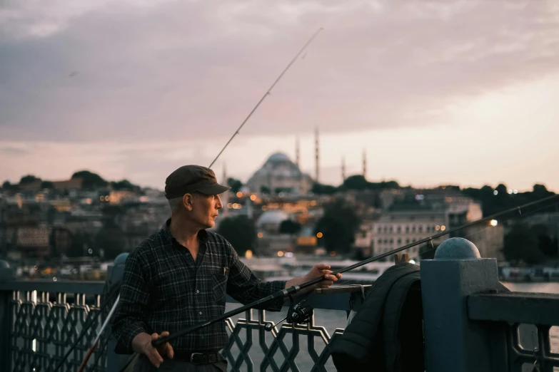 a man fishing on a metal railing in front of a city