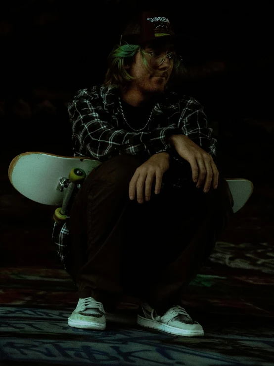 a young man holding a skateboard while sitting on the ground