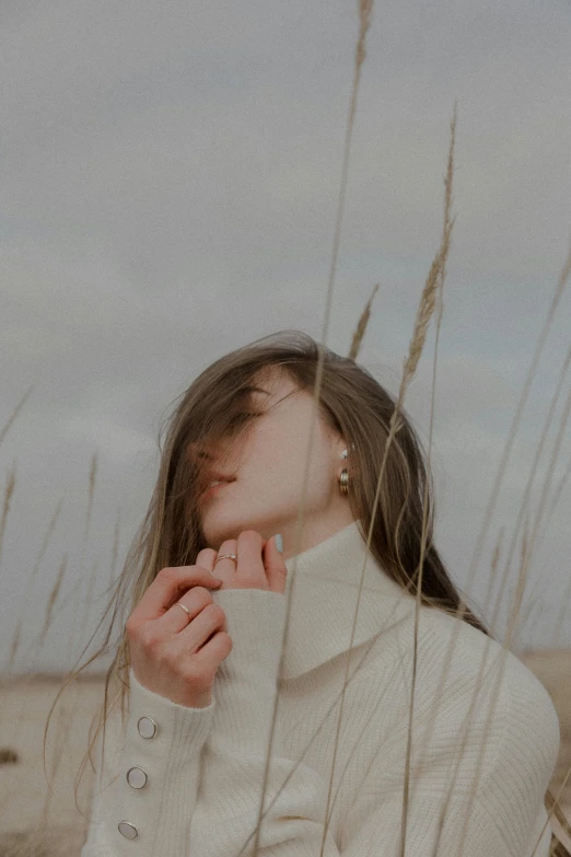 young woman in coat and earrings sitting amongst grass at the beach