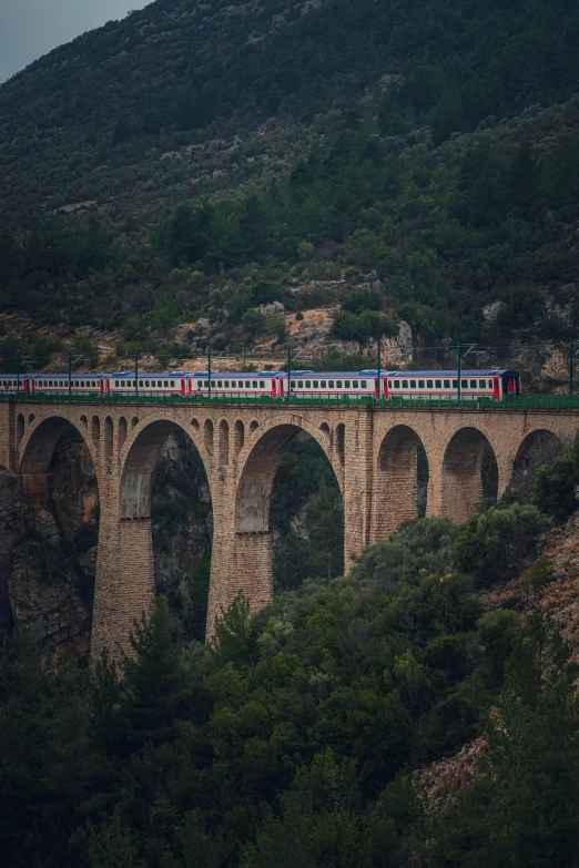 a long passenger train is travelling across an old stone bridge