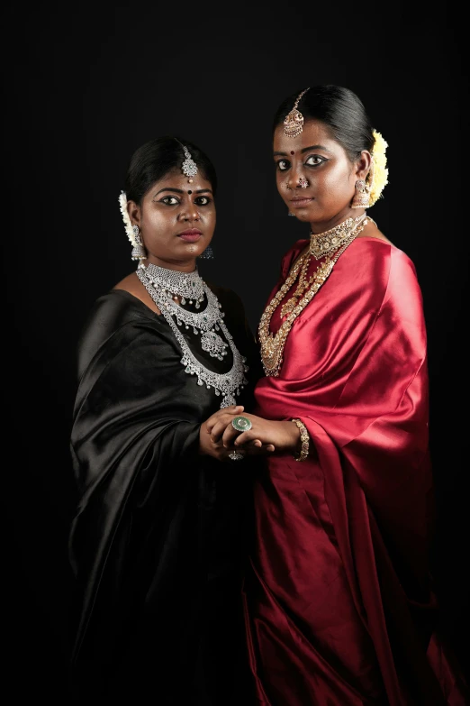 two women dressed in ethnic garb, both wearing their traditional attire and one has her arms around the other, and the other is facing forward