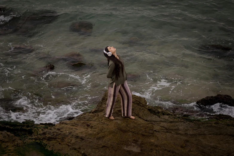 the woman is standing on the rock looking up at the ocean