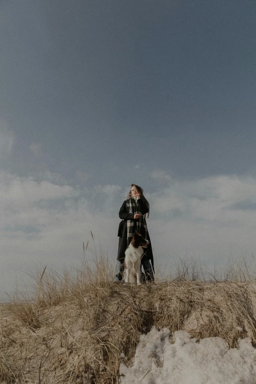 the girl is standing next to her dog on a hill