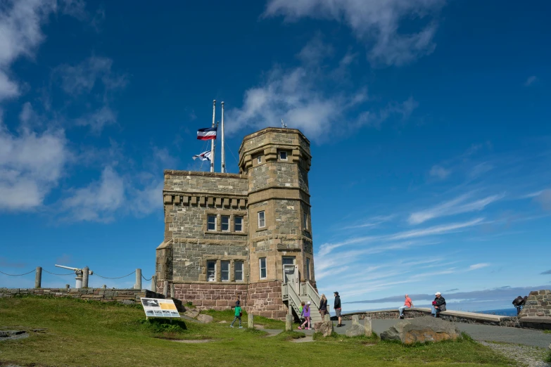 people standing outside a tall stone tower on a hillside