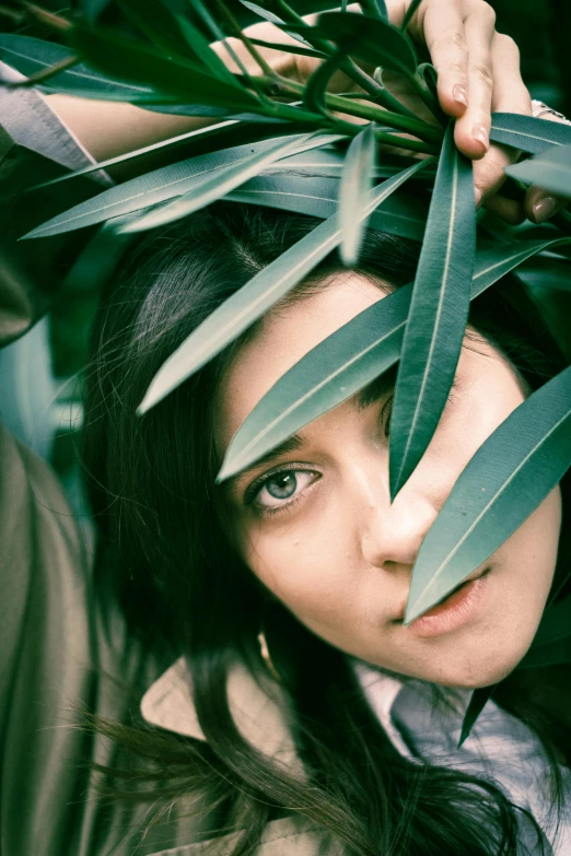 woman hiding her eyes behind green plants
