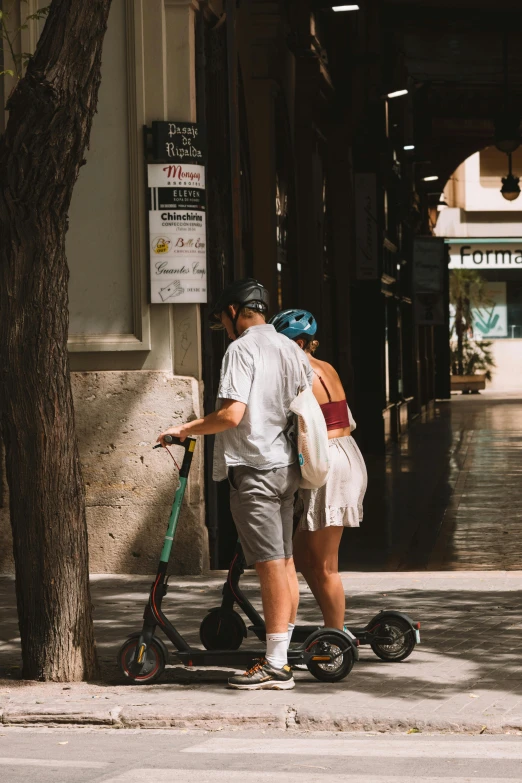 two people are standing on a scooter on the side of the road