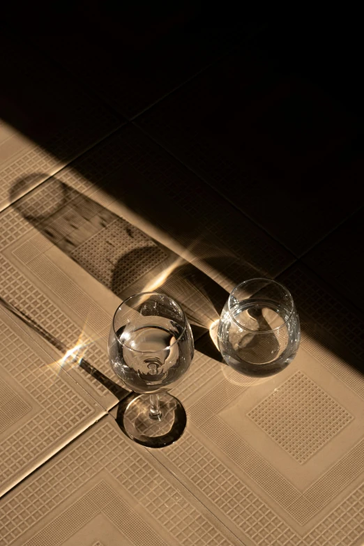 a pair of wine glasses on a table with a light shining in the background