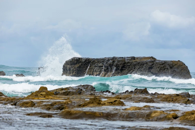 a wave crashing over some rocks on the beach