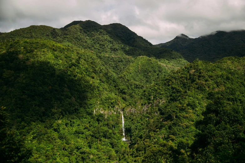 a waterfall surrounded by green hills on a cloudy day