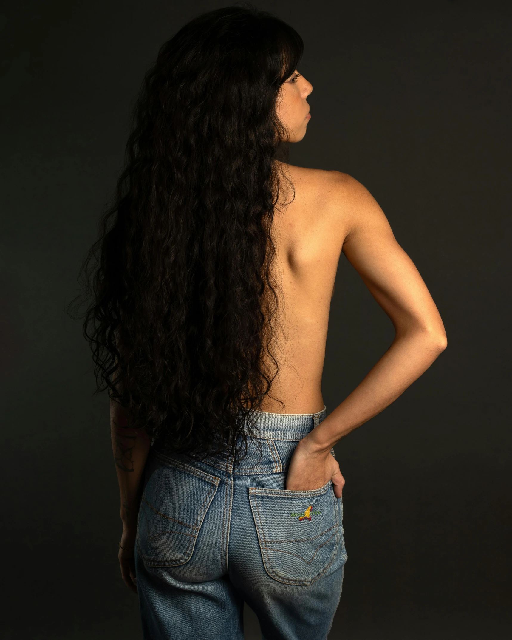 an extremely long curly haired woman posing with her back turned