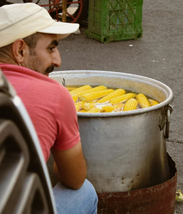 there is a man sitting on the ground looking at corn