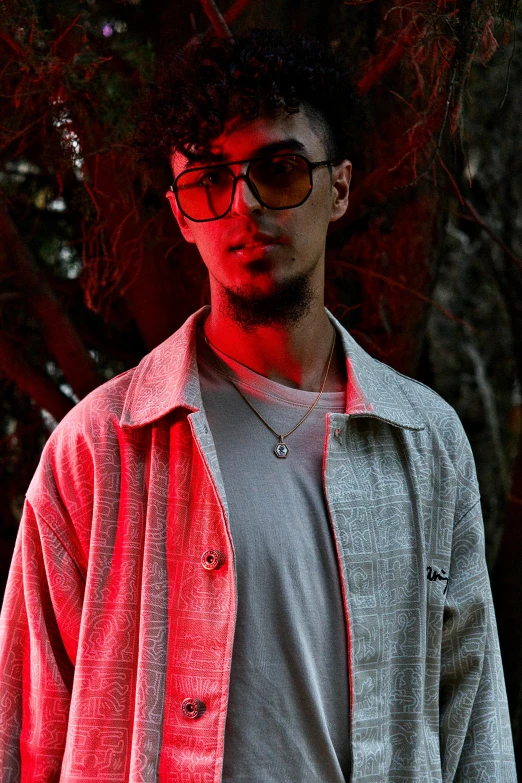 a man with glasses stands in front of some trees