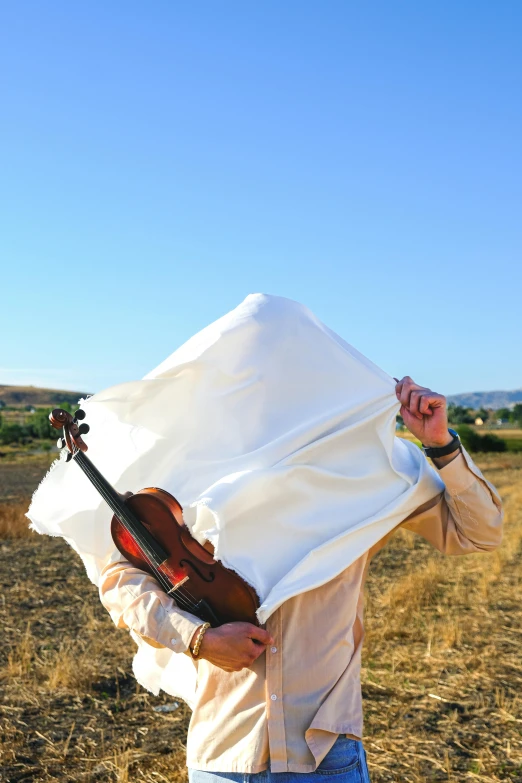 a man playing violin under a sheet in an open field