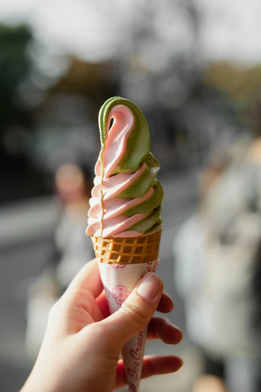 a person holds an ice cream sundae cone with green and pink icing