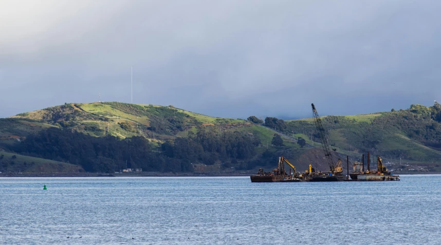 a ship sails past a tree - covered mountain in the distance