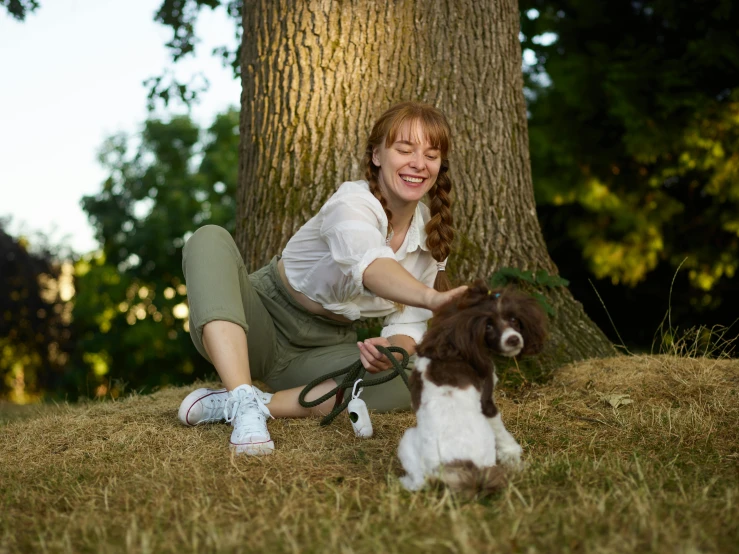 a woman is sitting on the grass with a dog