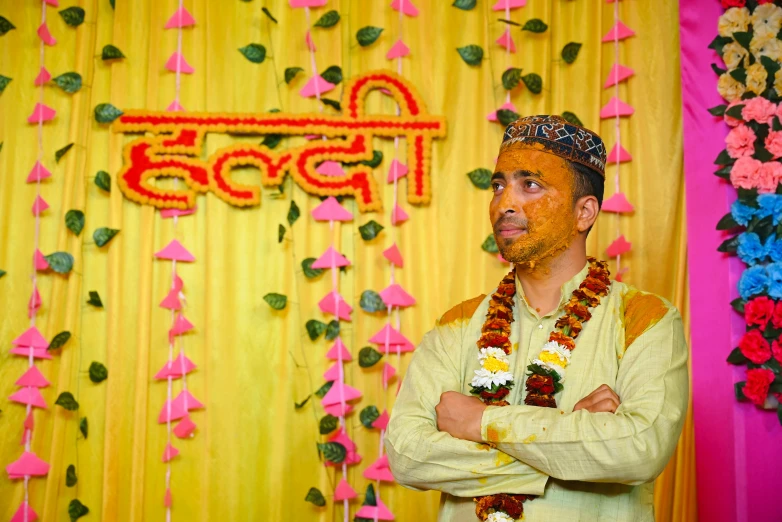 man with floral decorated headgear standing in front of yellow backdrop