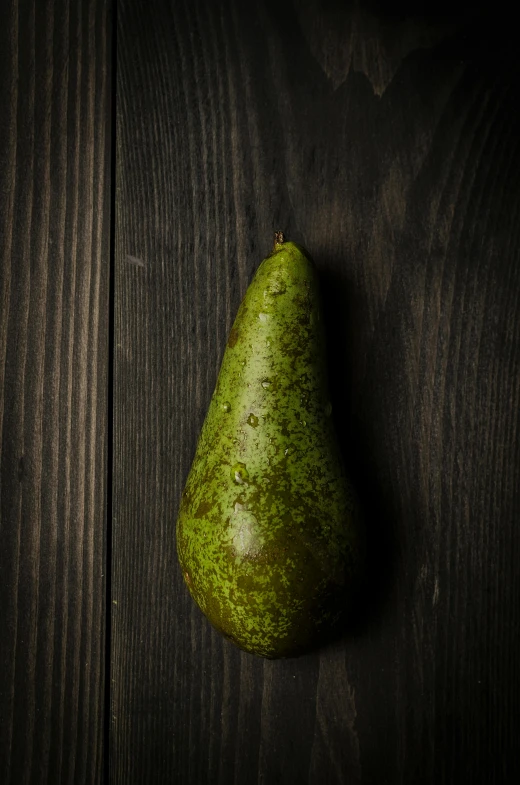 a green pear sits on top of a wooden table