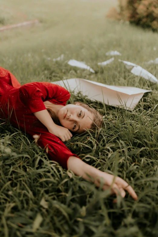 a woman lying in grass next to a paper boat