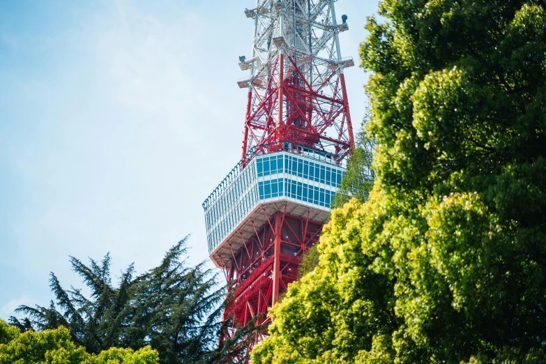 a tall tower with a red structure sitting behind some trees